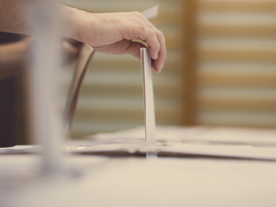 Hand placing a piece of paper into a ballot box