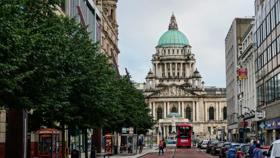 Photo of a main road in Belfast, with a large white building in the background and a tarmac road in the foreground.