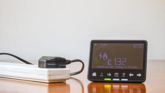 A smart meter on a wooden floor with a plug extension to the left.