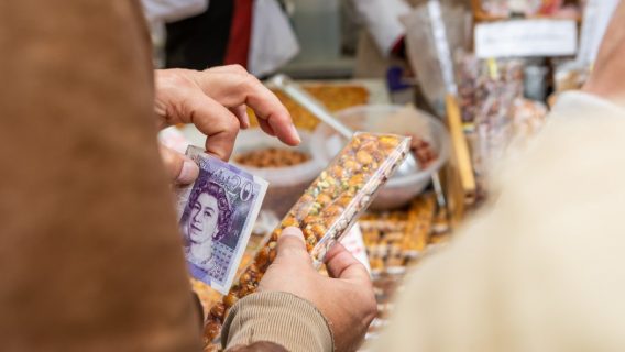 Image shows a person paying for a food item with a £20 note.