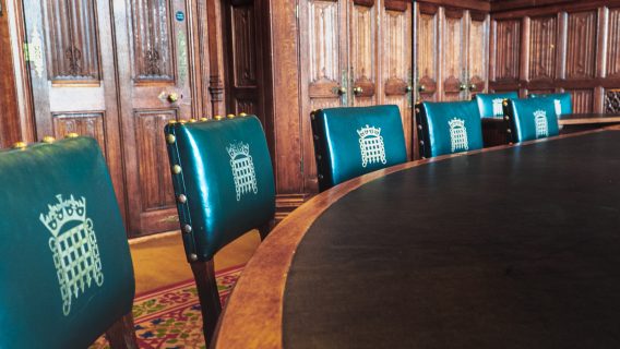 Image shows a row of green leather chairs with portcullises on the headrest surrounding a curved wooden table